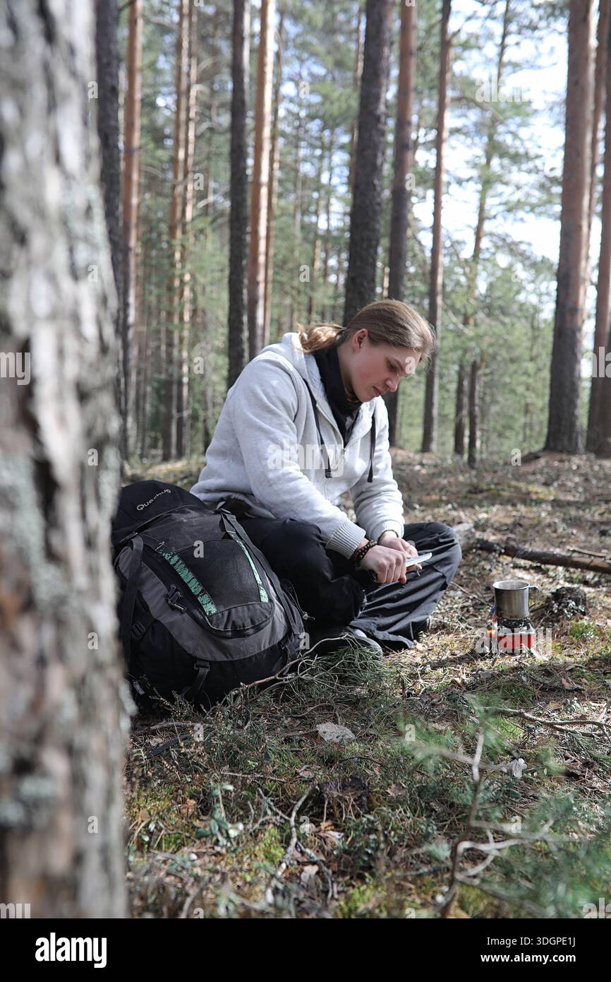 A man in a campaign drinks tea. A young traveler in the woods camped and cooked breakfast in nature. The naturalist drinks hot fresh tea cooked on ope Stock Photo