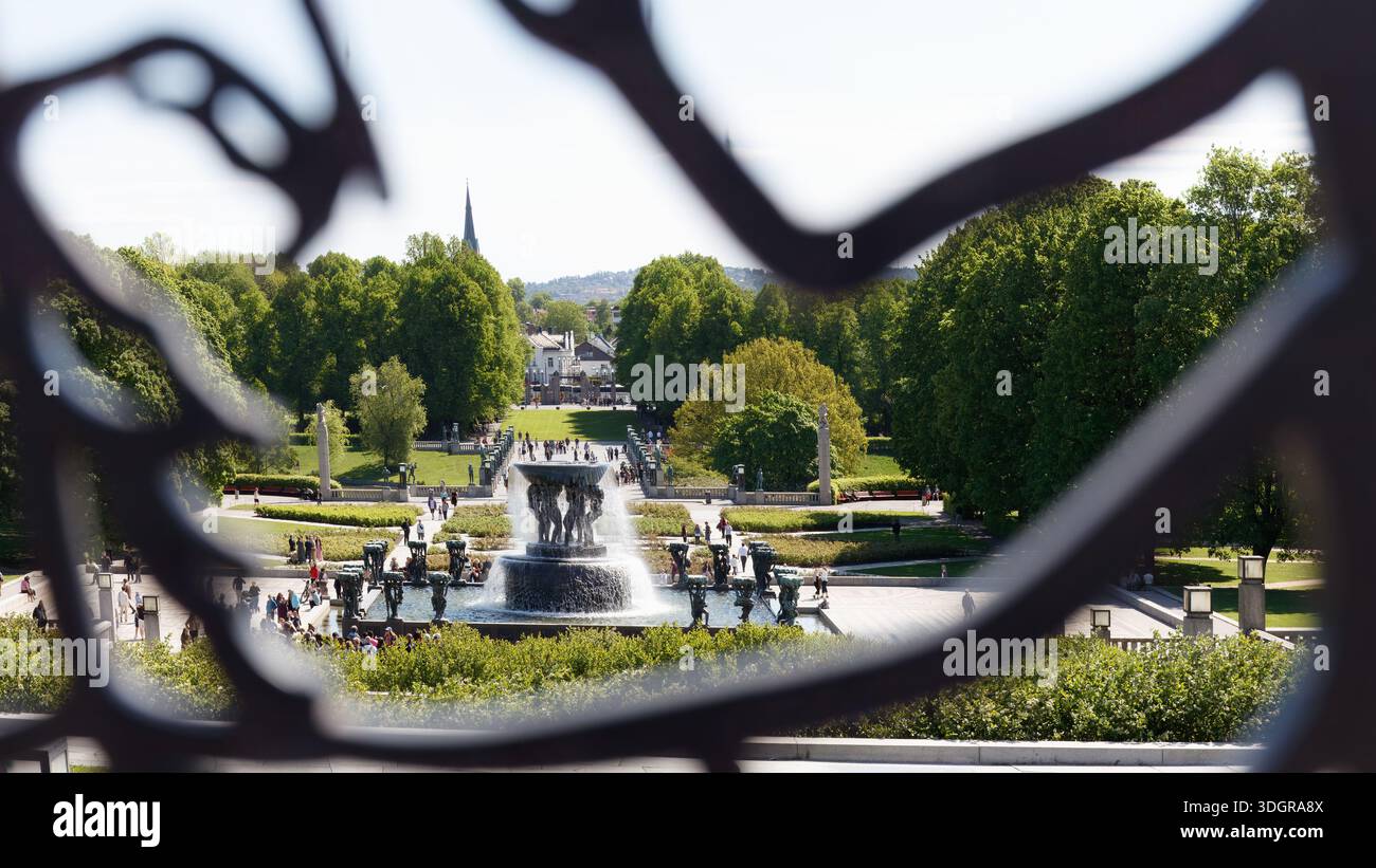Oslo, Norway - May 18, 2025: View of Vigeland Park landscape framed by a metal sculpture, showcasing the fountain and trees with people walking in the Stock Photo