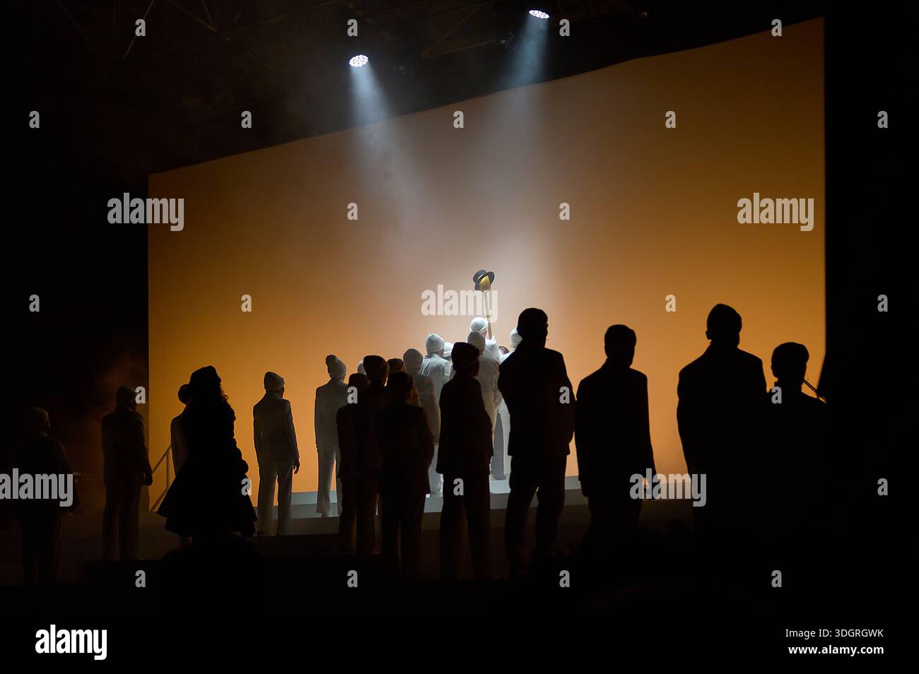 A striking theatrical scene featuring a large cast in white suits and a woman in red amidst dramatic stage fog and professional lighting. Stock Photo