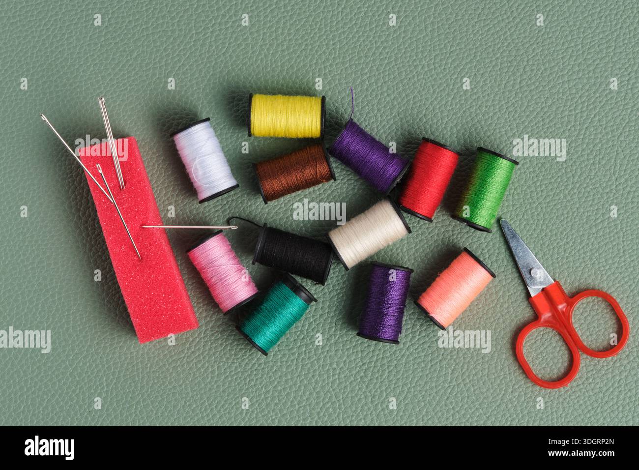 Spools of thread, scissors and needle on green background Stock Photo