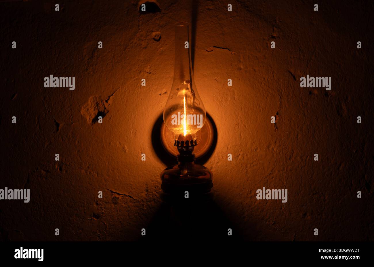 Burning oil lamp casting warm light and deep shadows on dark wall ...