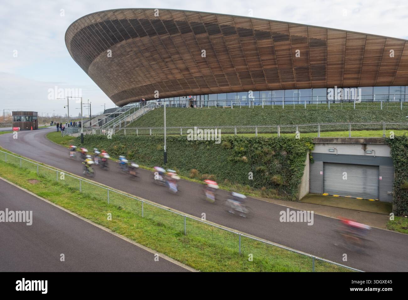 Blurred road cyclists racing on an outdoor bike track with the Lee Valley Velodrome in the background. Queen Elizabeth Olympic Park, Stratford, E20. Stock Photo