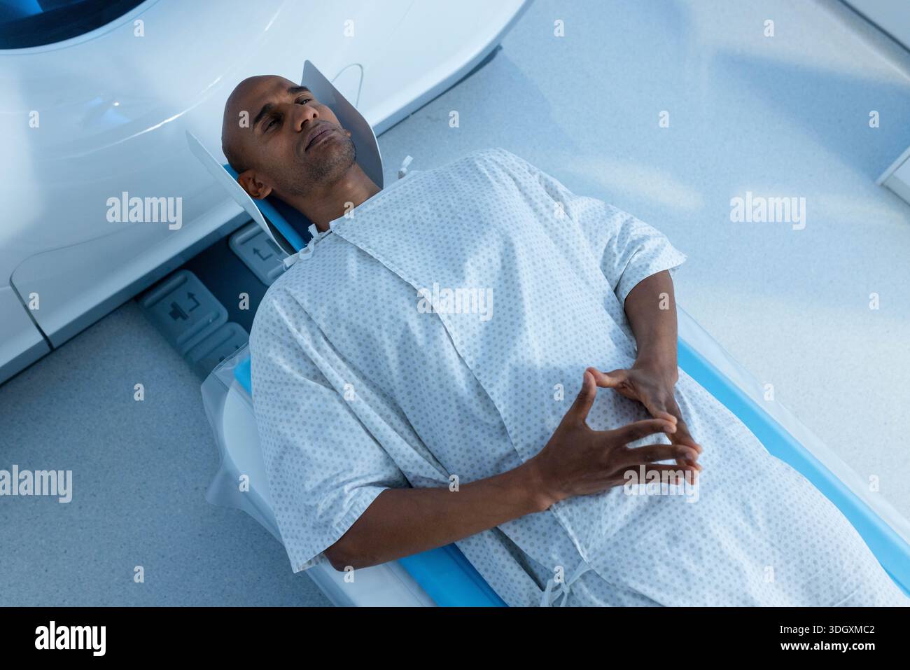 Male patient lying supine in gantry on table with head support in radiology suite, wearing gown. Scanner, imaging, diagnostic, medical, hospital, clin Stock Photo