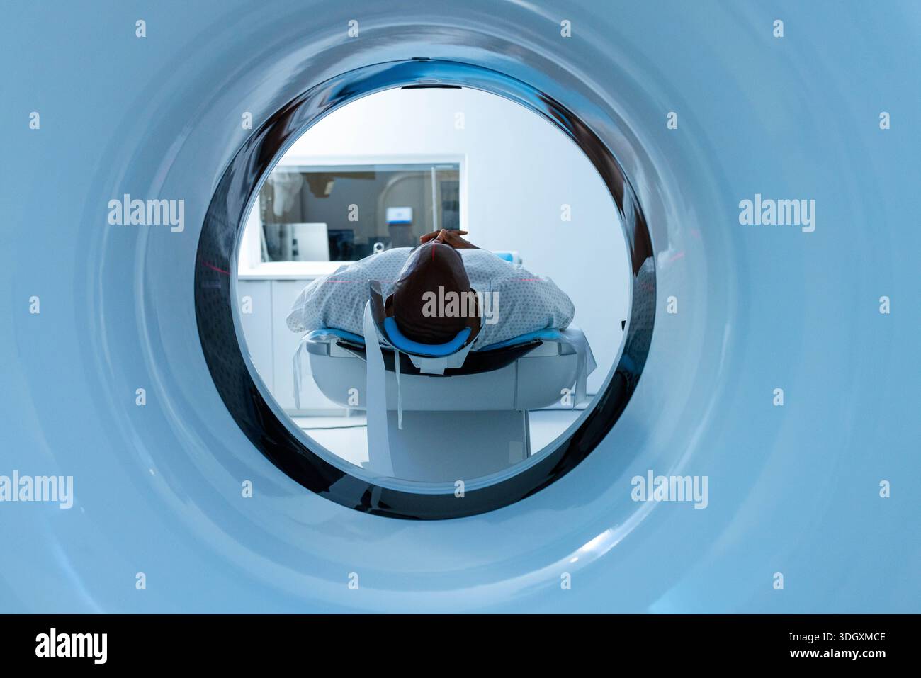 African American woman lying on scanner table at hospital, wearing patterned gown and foam headrest. Gantry, imaging, radiology, diagnostic, sterile, Stock Photo