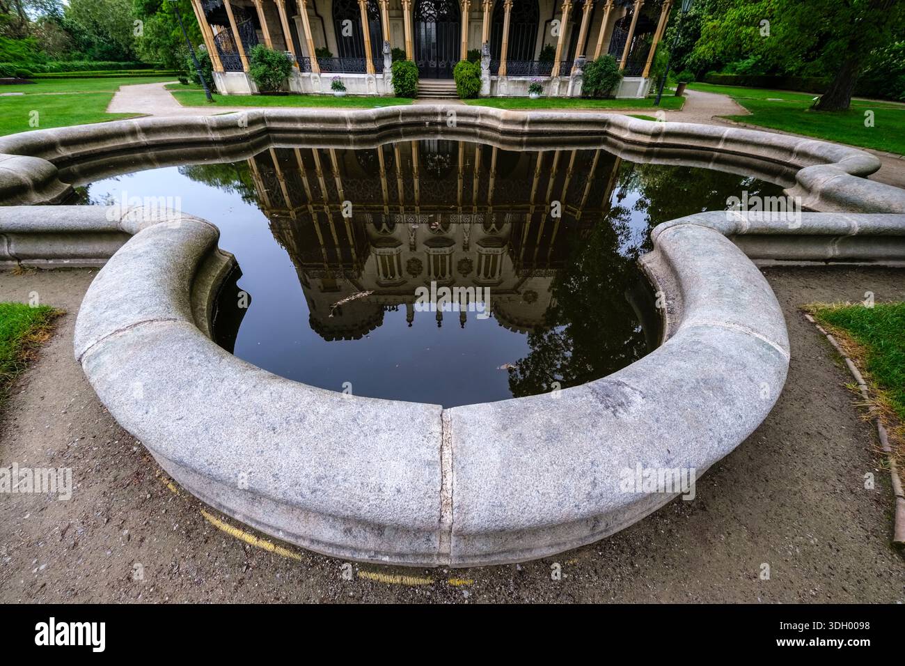 Stone-rimmed pond reflecting the ornate facade of Hluboká Castle, with the building's lower level and ironwork visible in the distance. Stock Photo