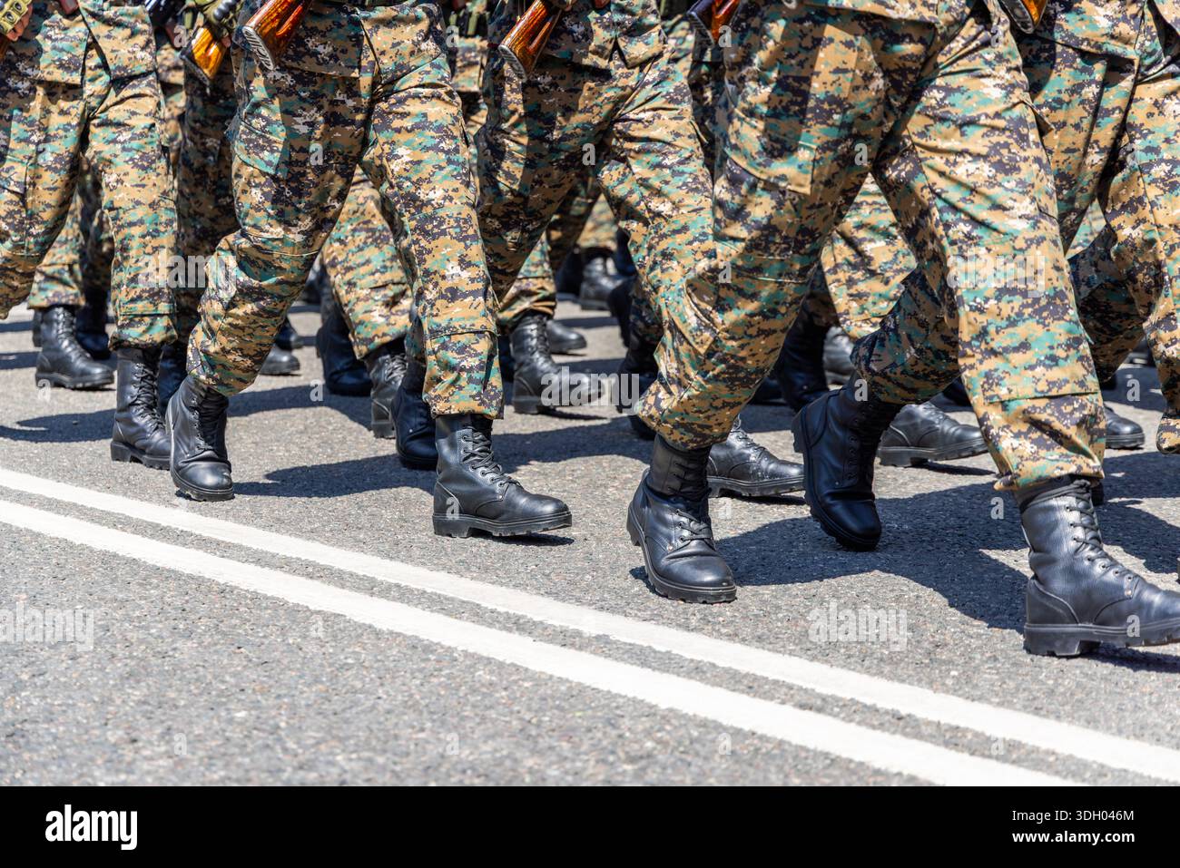 Group of soldiers in camouflage uniforms marches with rifles on paved ...
