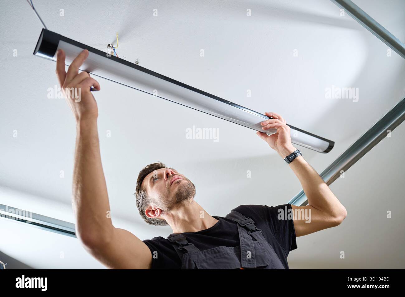 Man in workwear installing a linear LED light fixture on the ceiling ...