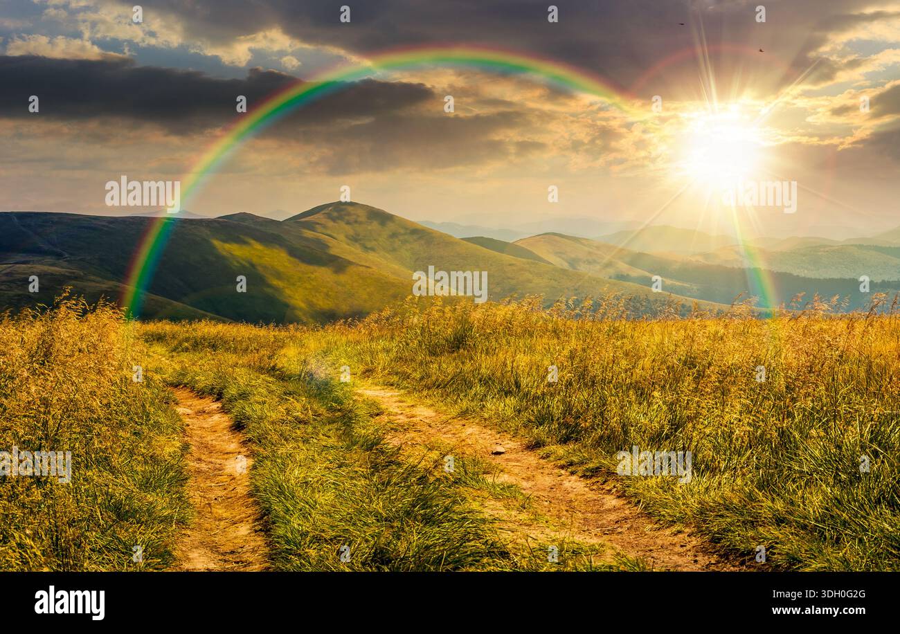 dirt road through grassy alpine meadow on the ridge at sunset. beautiful summer landscape in green mountains under cloudy sky in evening light. timele Stock Photo
