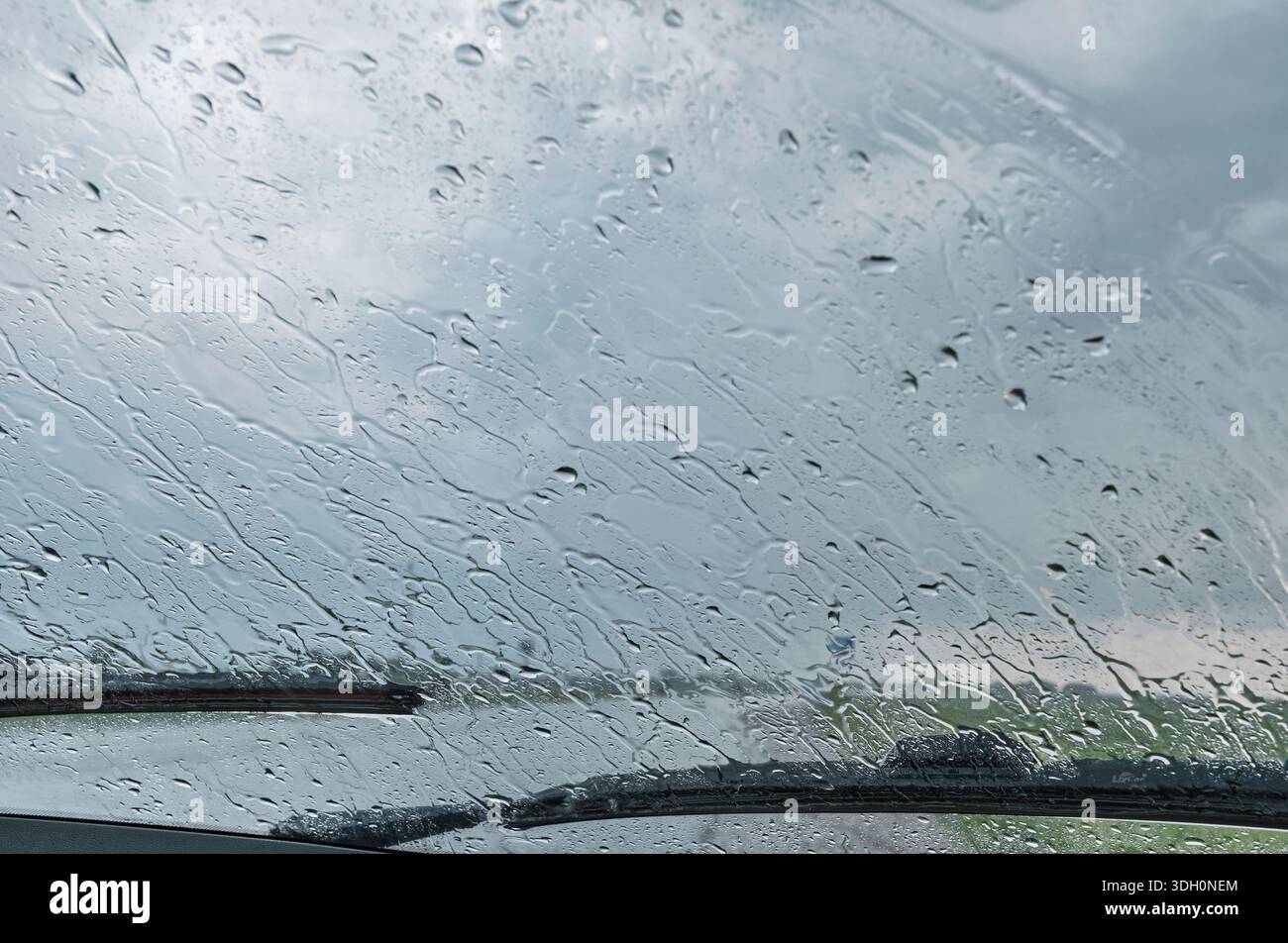 Raindrops on car windshield with wipers and cloudy sky background Stock Photo