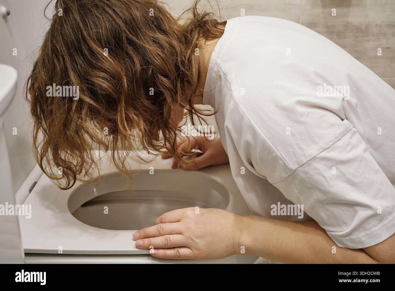 Woman experiencing sickness and stomach pain, leaning over toilet bowl Stock Photo