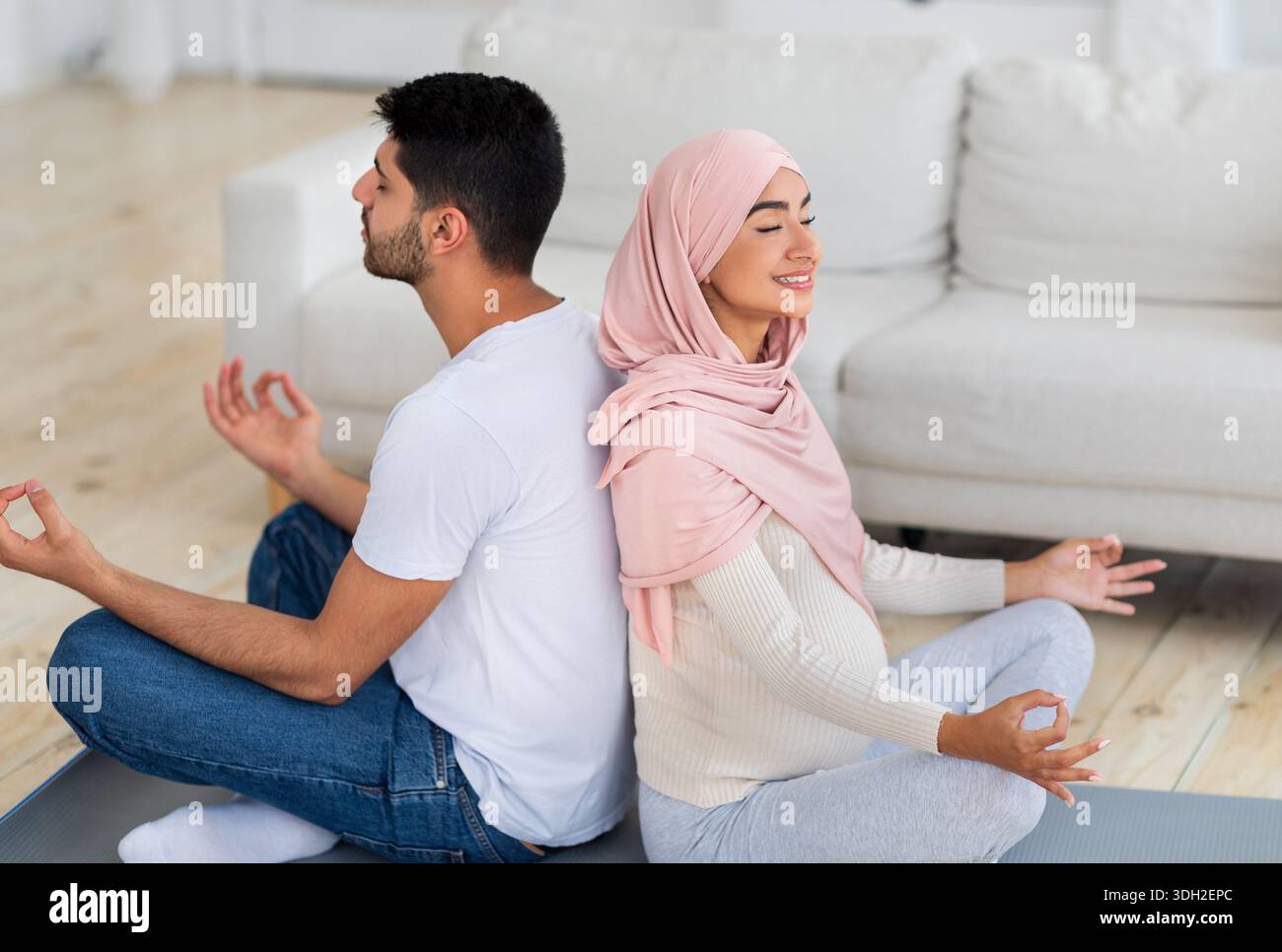 Yoga for pregnancy. Happy muslim spouses meditating together at home, sitting back to back and practicing lotus pose Stock Photo