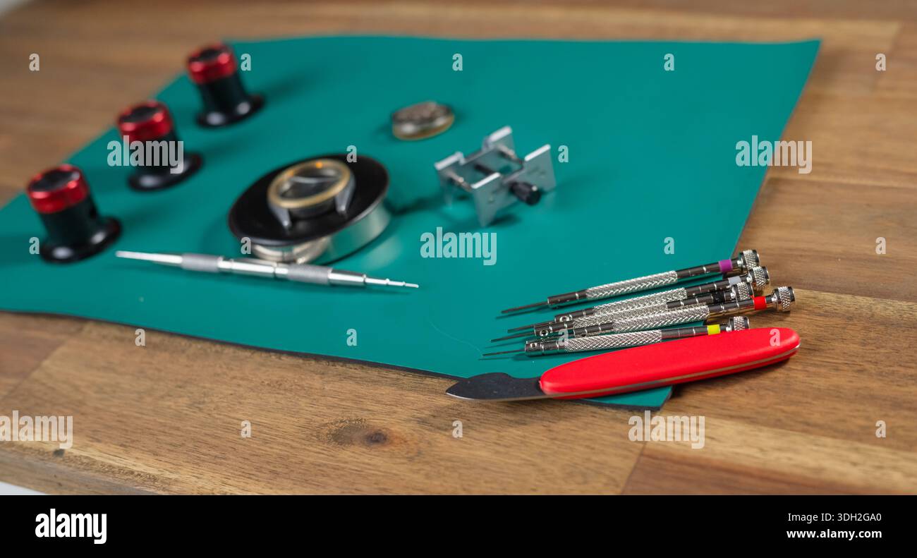 A watchmaker prepares tools for the repair of a mechanical watch on a green surface with various instruments. Stock Photo