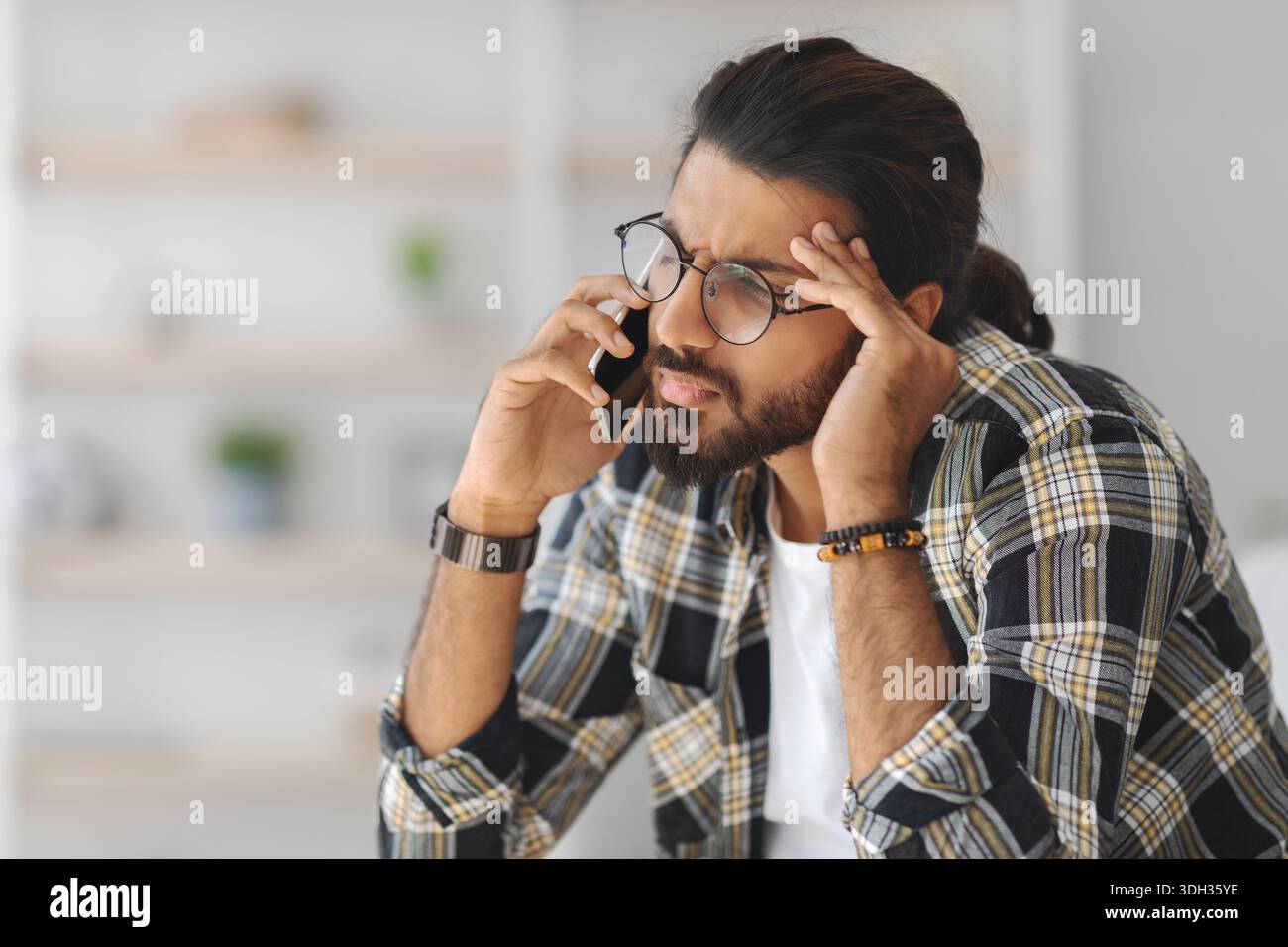 Upset middle-eastern guy having phone conversation, home interior Stock Photo
