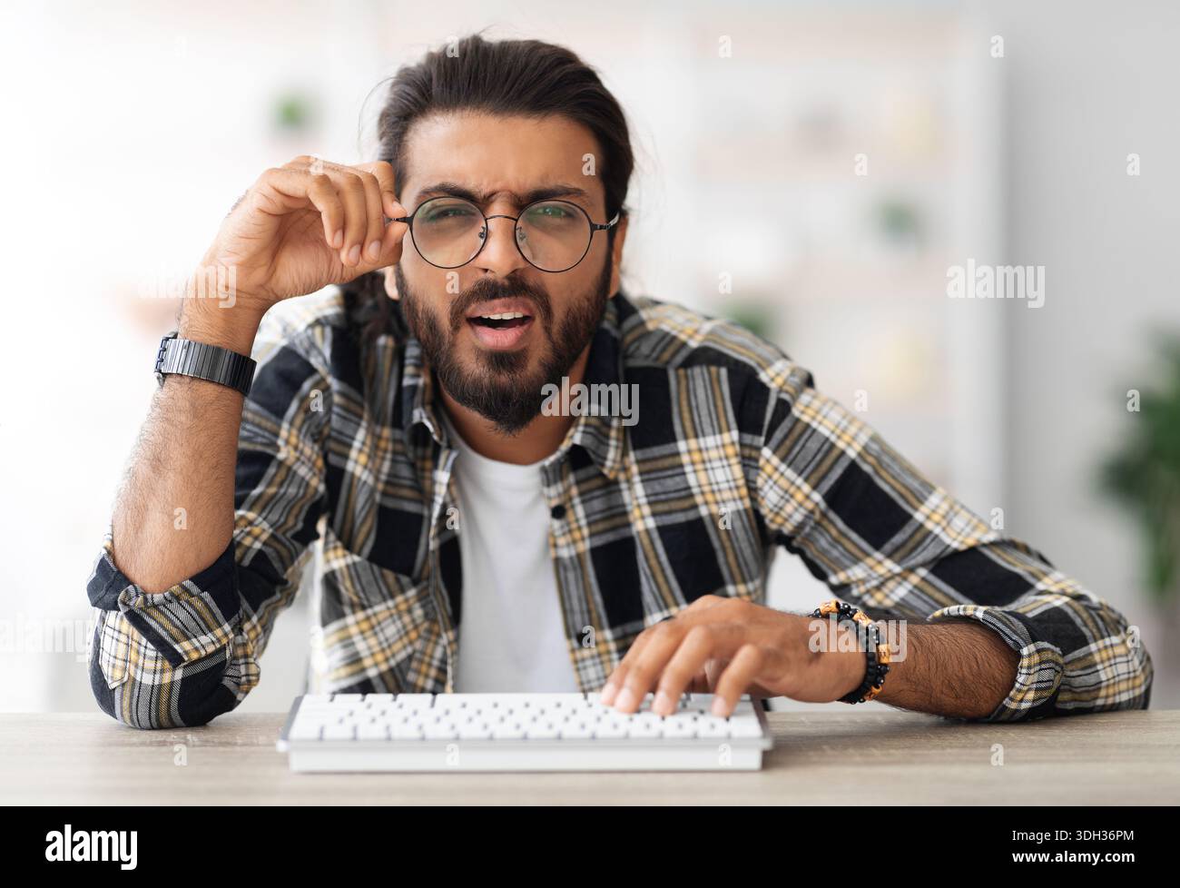 Confused middle-eastern man programmer sitting at worktable, touching glasses Stock Photo