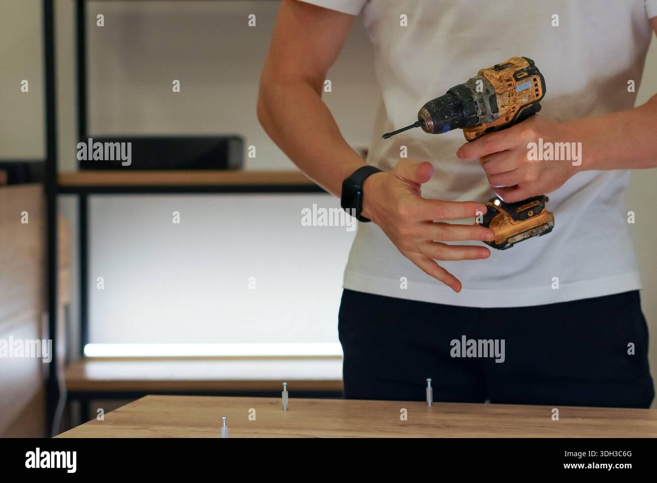 Individual using fingers to guide screw while holding drill in workshop environment Stock Photo
