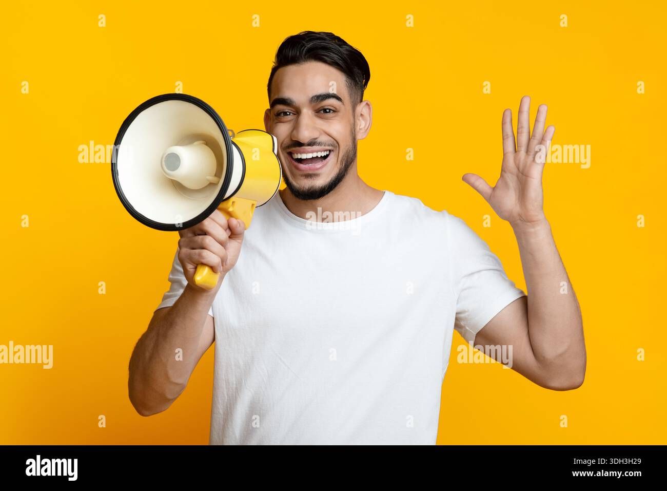 Excited arab guy speaking loud, using megaphone on yellow Stock Photo