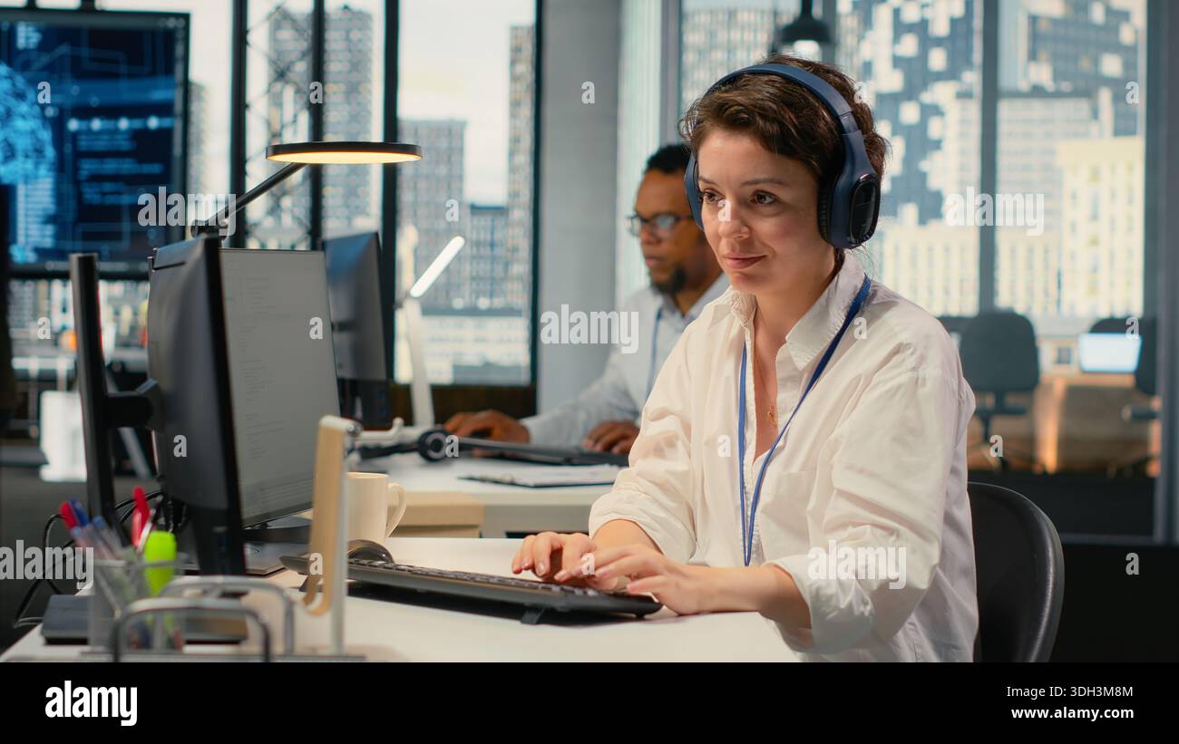 Developer listening music while working in AI startup training predictive models for language processing tasks. Tech expert wearing audio headphones uses technical expertise for IT tasks, camera B Stock Photo