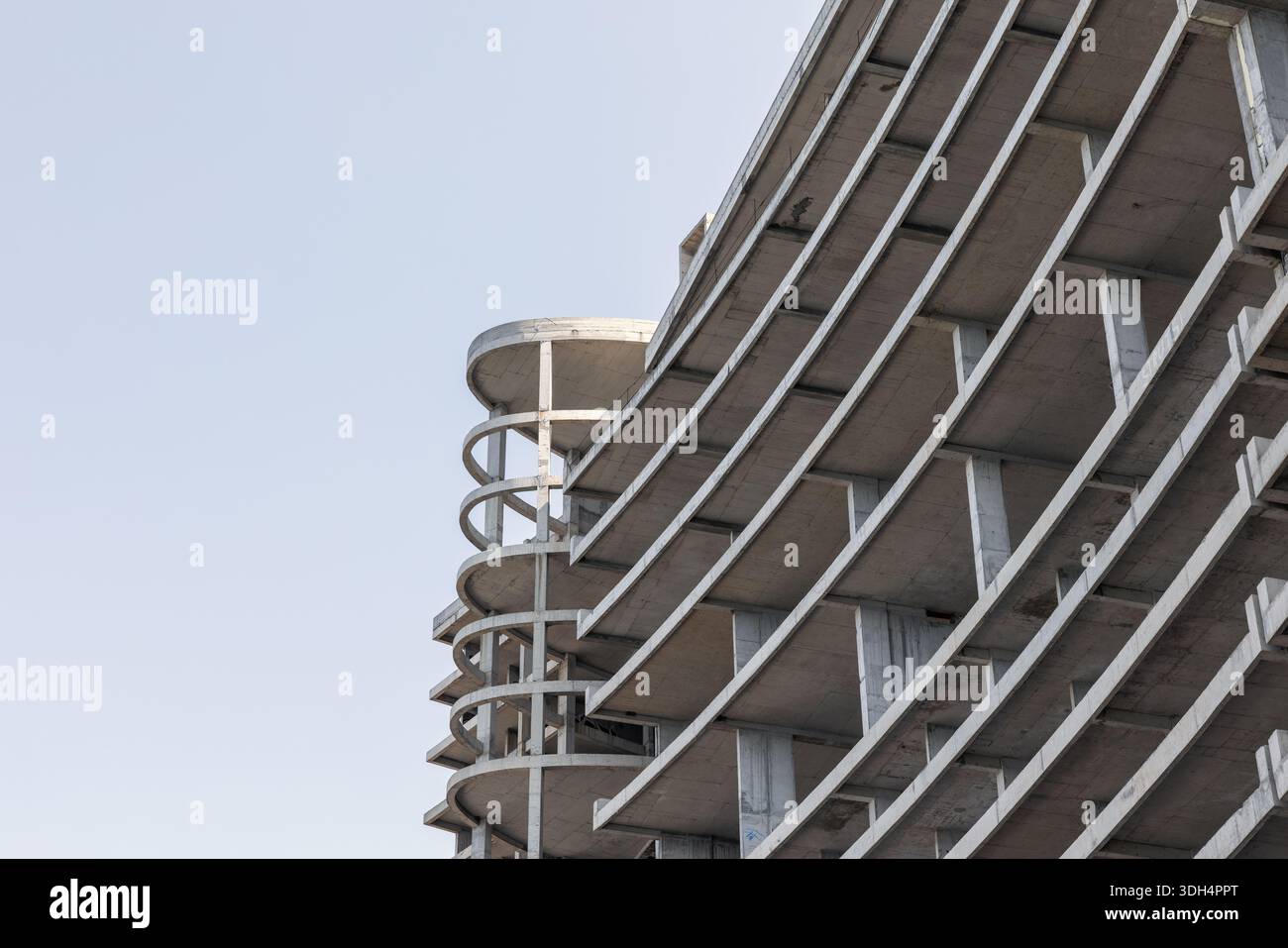 A concrete building under construction rises with circular ramp columns ...