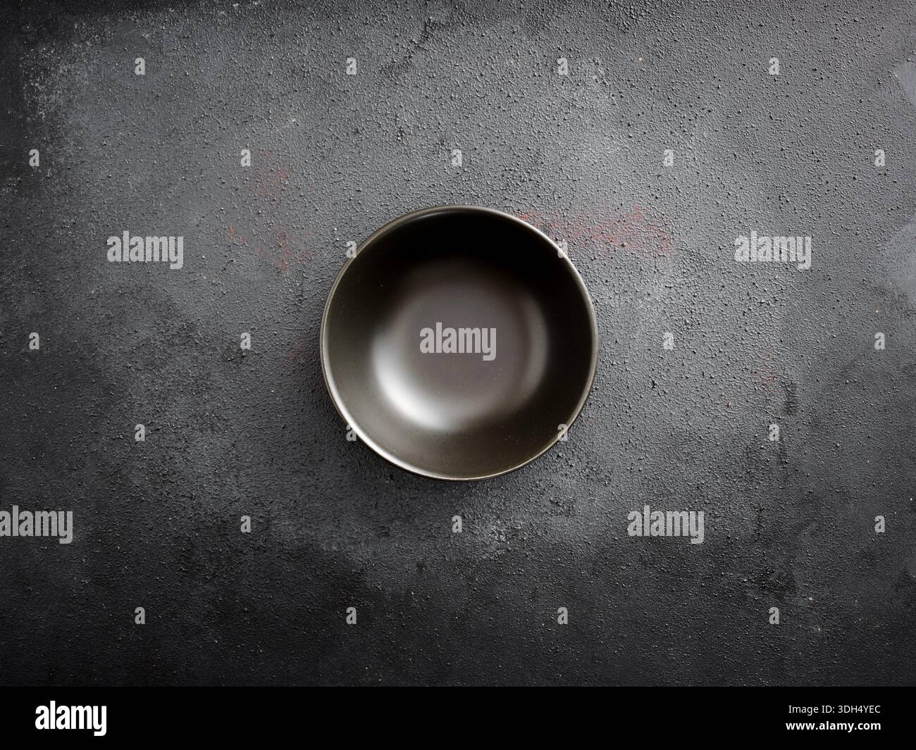 Empty black ceramic bowl centered on a dark grey concrete table with rough texture. Minimalist and top view Stock Photo