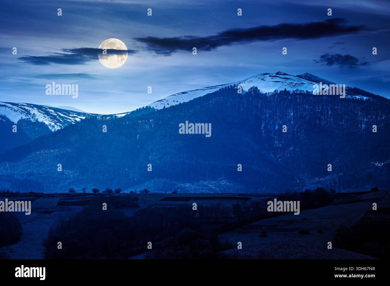 carpathian mountains of ukraine in early spring at night. view of countryside landscape with rolling hills and snow covered peak in full moon light. i Stock Photo