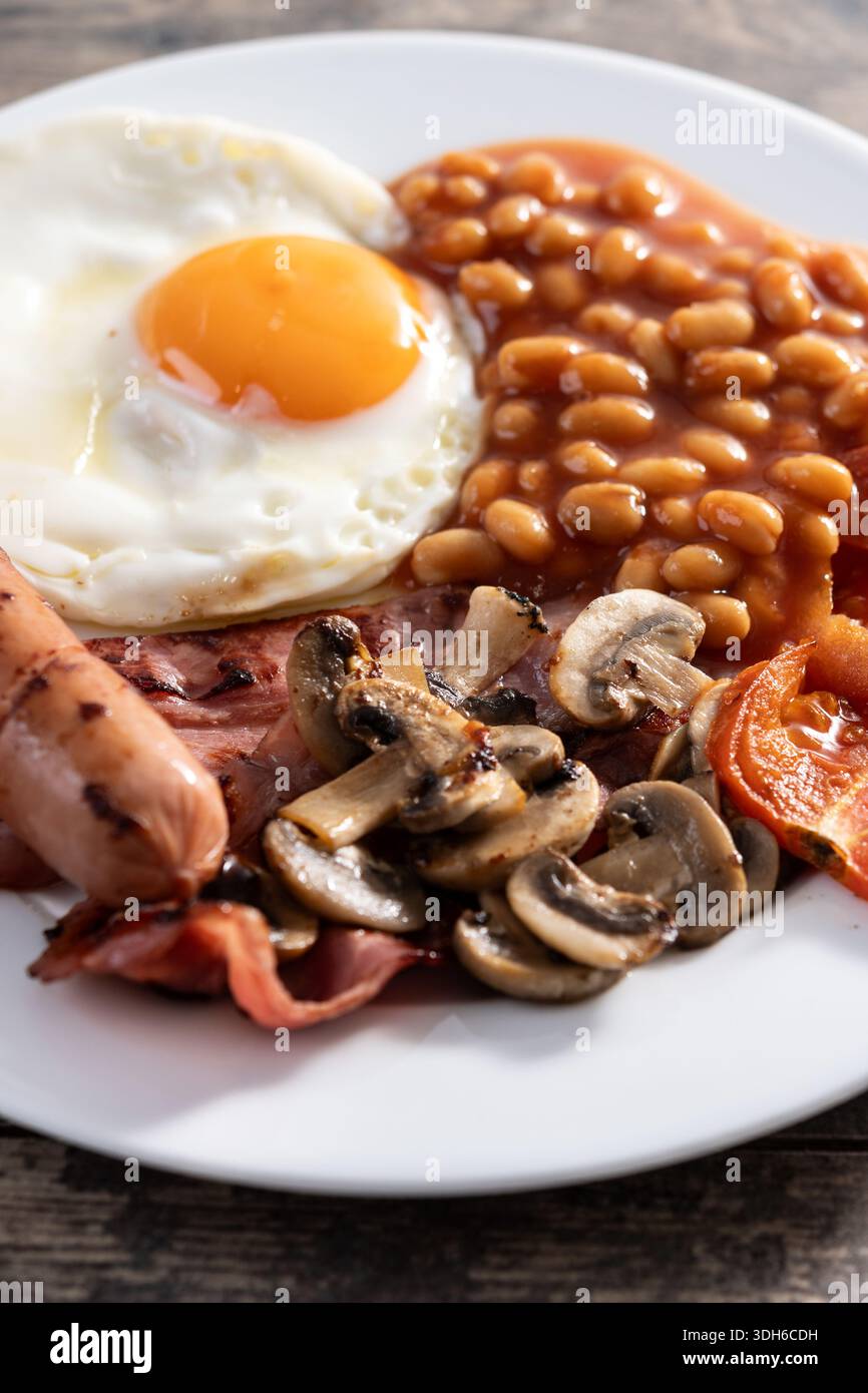 Full English breakfast with fried egg, bacon, sausages and beans on wooden table Stock Photo