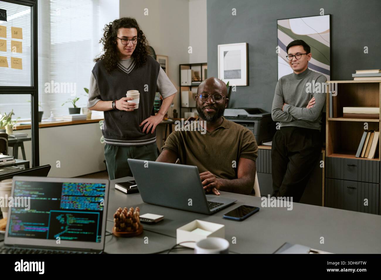 Young Black Man Smiling While Working on Laptop with Diverse Coworkers Stock Photo