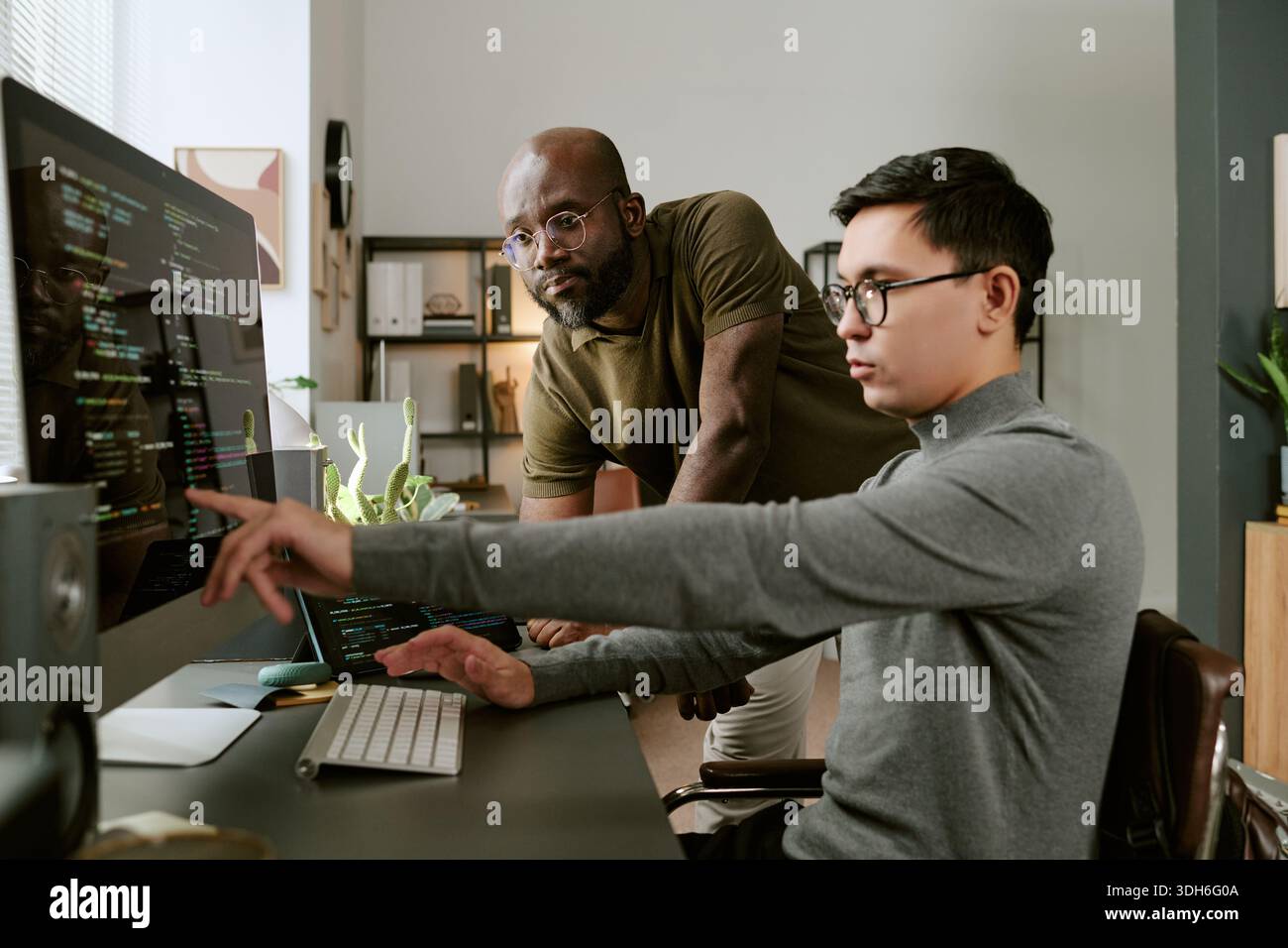 Young Asian Man Collaborating with Young Black Man While Coding Software Stock Photo