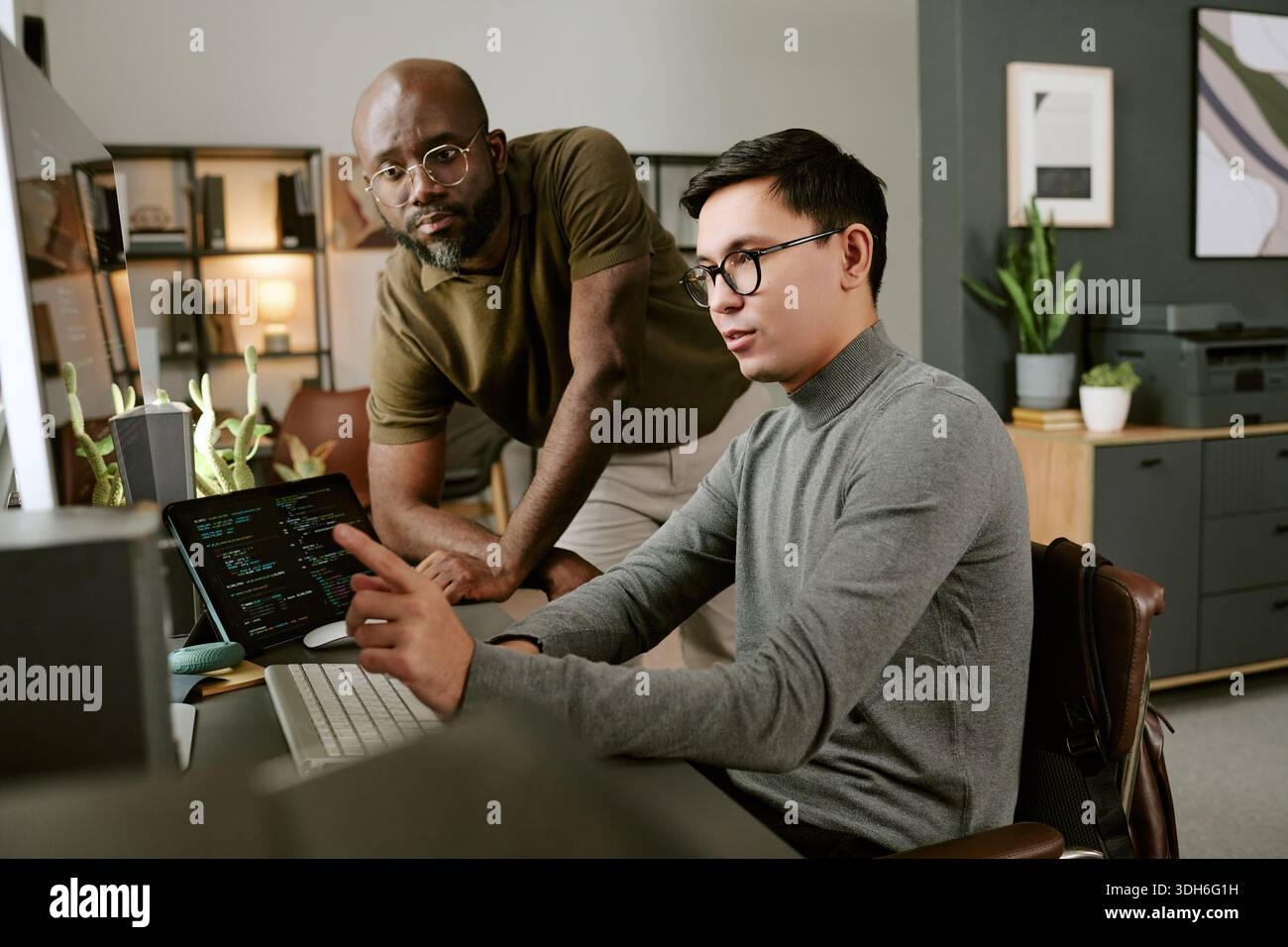 Young Man Explaining Code to Young Black Man in Office Setting Stock Photo