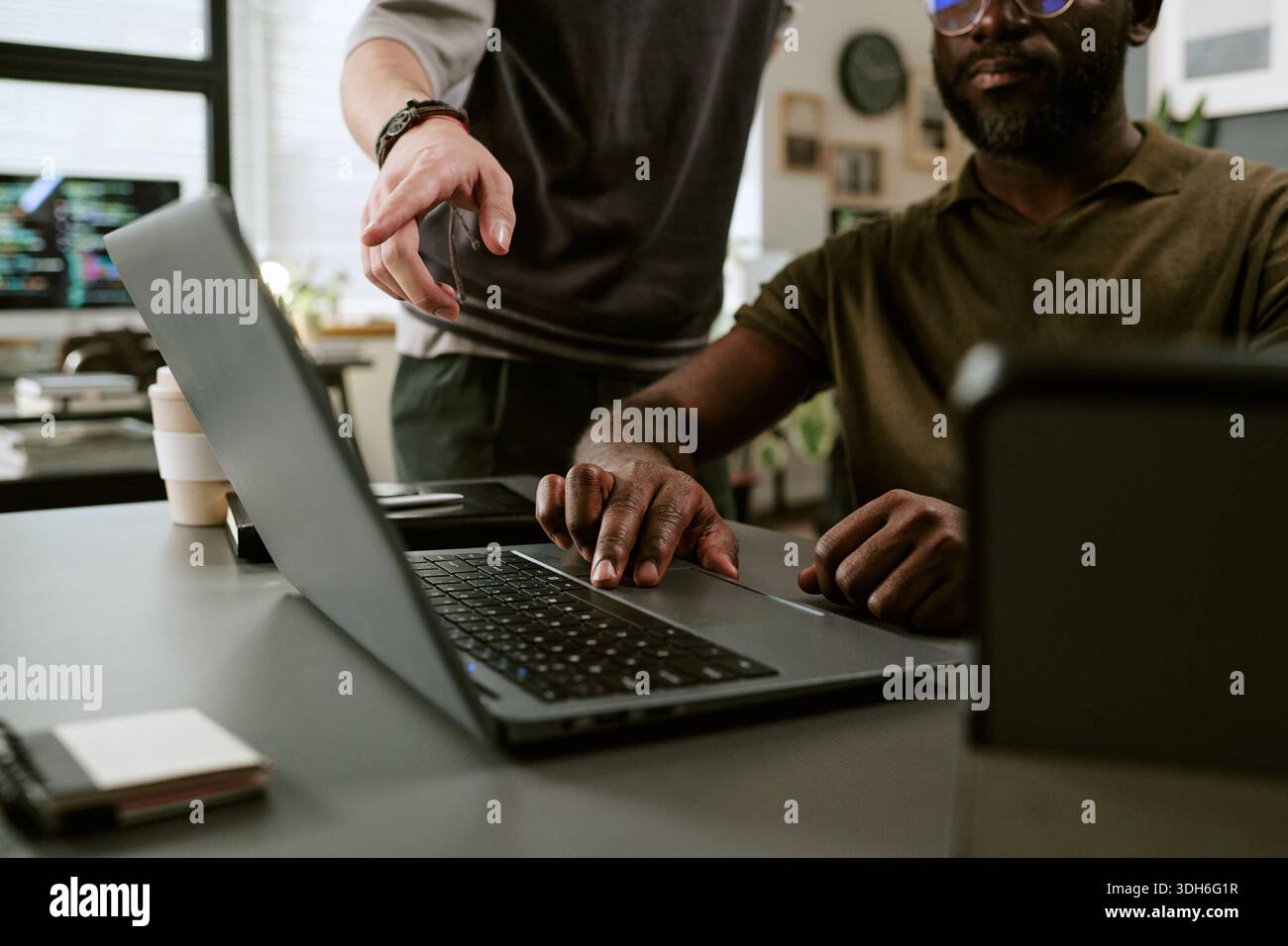Young Black Man Using Laptop While Colleague Pointing at Screen Stock Photo