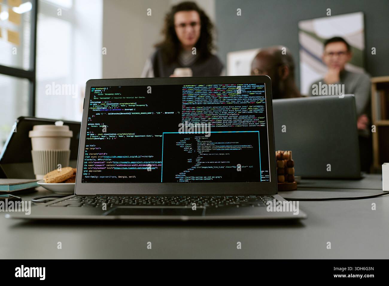 Young Adult Men Collaborating in Office While Laptop Displaying Programming Code Stock Photo