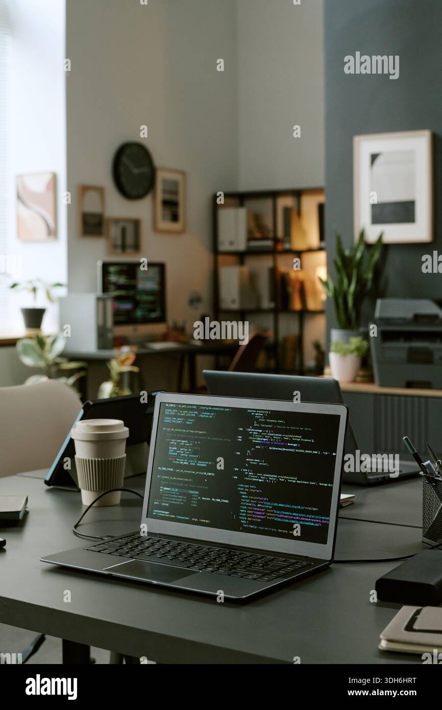 Modern Office Workspace Featuring Laptop Displaying Programming Code Stock Photo