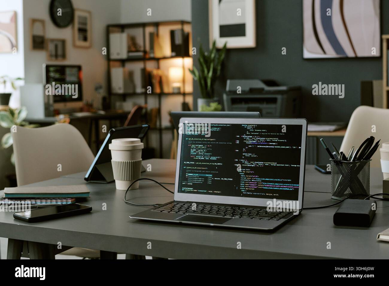 Modern Office Workspace Featuring Laptop Displaying Programming Code on Screen Stock Photo