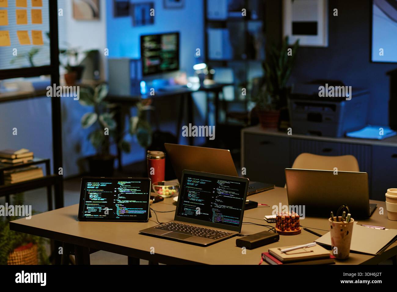 Empty Office Workspace Featuring Multiple Laptops Displaying Programming Code Stock Photo