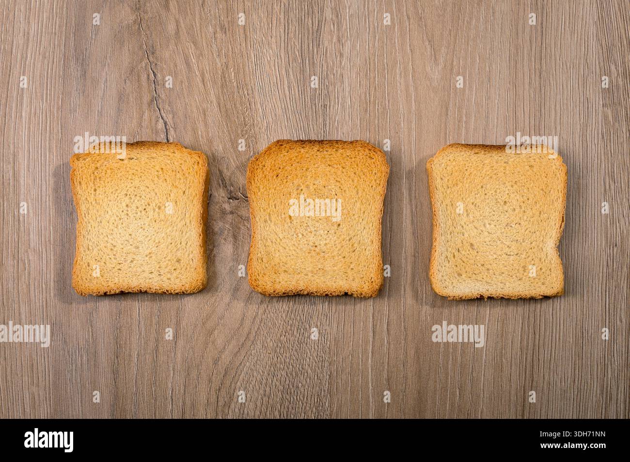Three slices of dried bread or rusks lying flat on a light wooden background Stock Photo