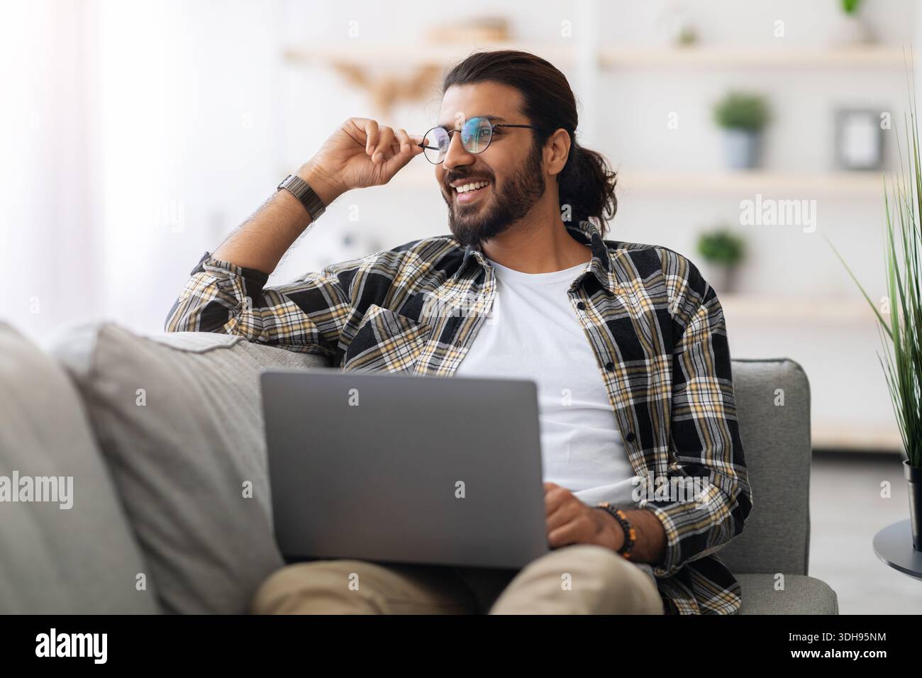 Dreamy arab guy freelancer working from home, using laptop Stock Photo
