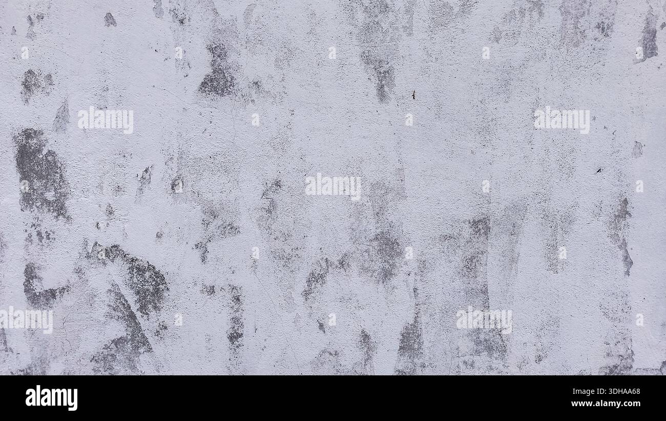 A high-resolution, close-up shot of a weathered, light-colored wall with visible gray patches, cracks, and peeling paint, creating a gritty, industria Stock Photo