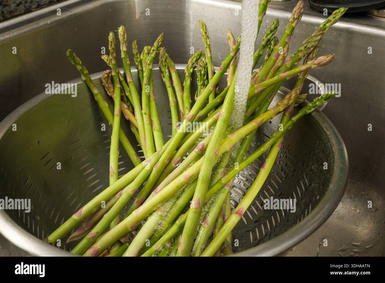Close-Up of Rinsing Asparagus Spears Under Faucet in Colander Stock Photo