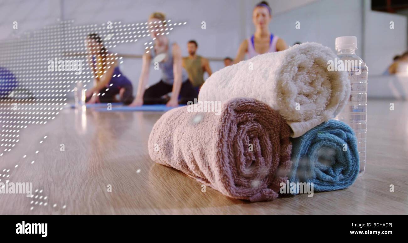 Stacking three rolled towels and water bottle on yoga studio floor, with mats, people in activewear Stock Photo