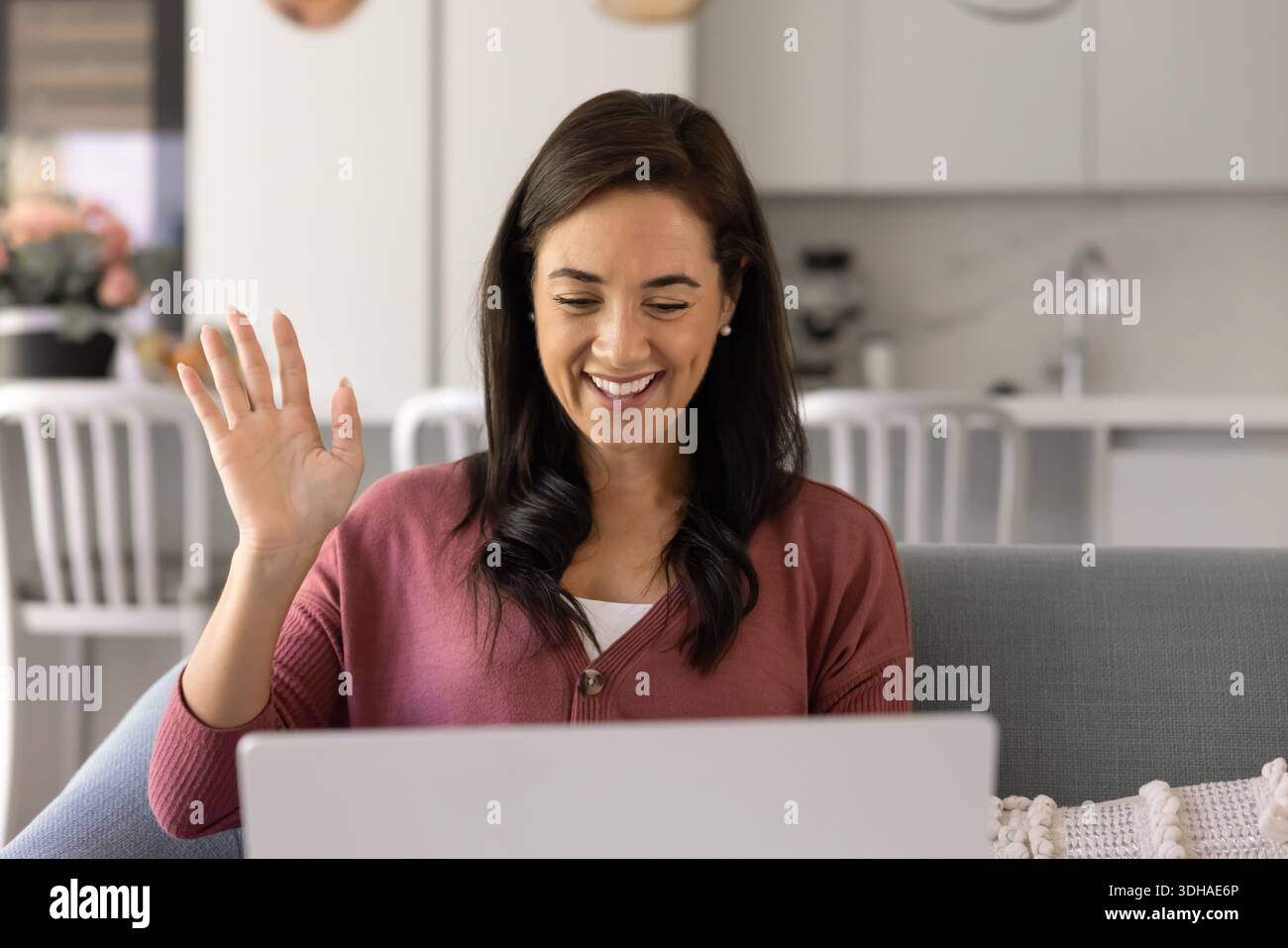 Happy woman sitting on sofa, waving, start video conference Stock Photo