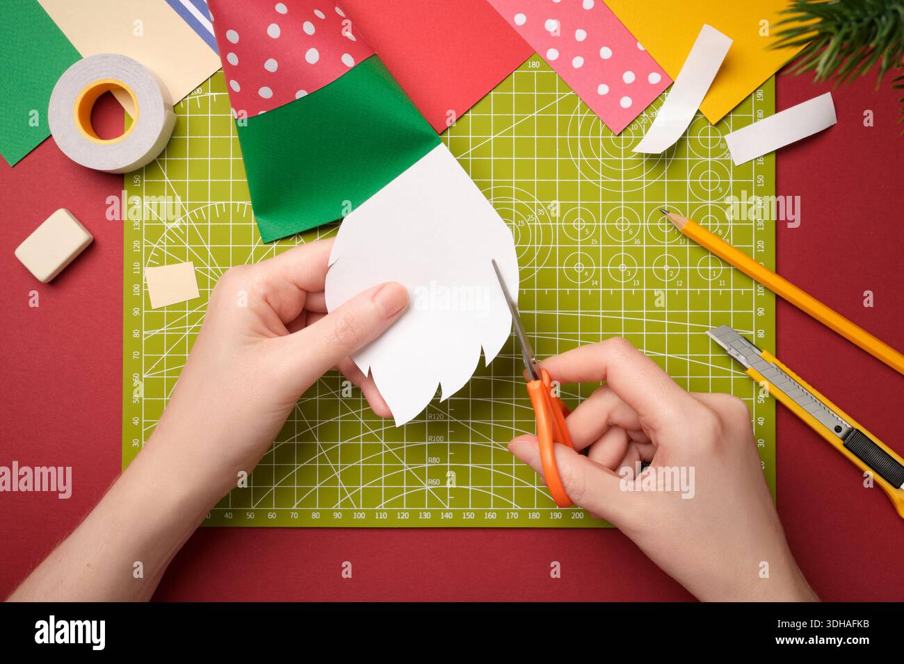 Making a gnome craft. Hands cut out a beard from white paper. Creative process. Stock Photo