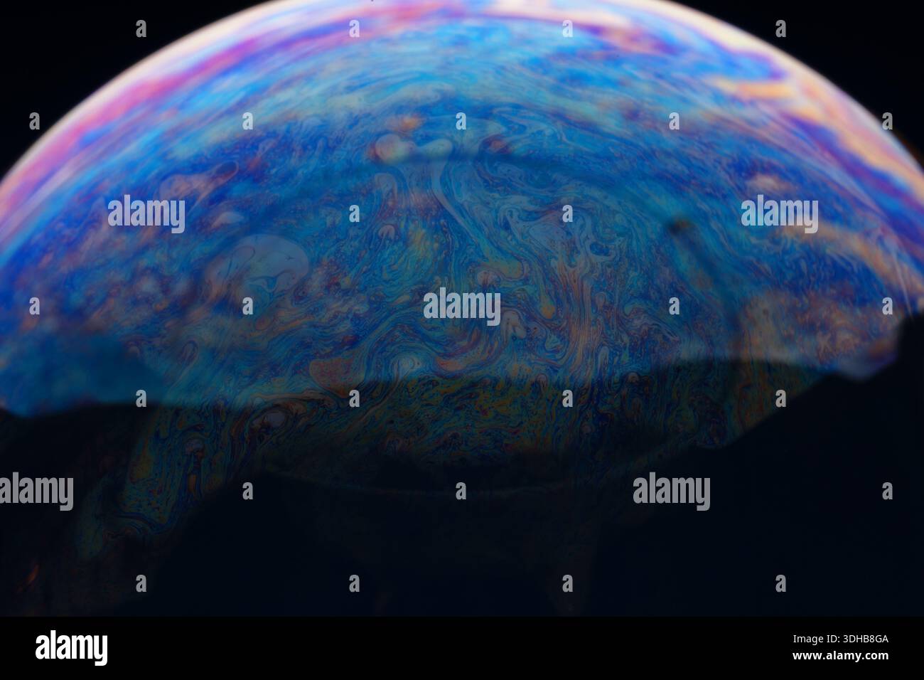 Close-up of a soap bubble with vibrant, swirling patterns and colors on a dark background, ideal for creative concepts and backgrounds. Stock Photo