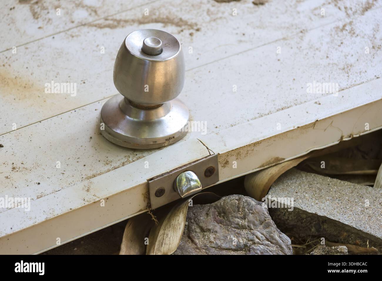 Close up view of old silver metal doorknob on broken white wooden door lying on ground abandoned outdoors creating lonely and neglected atmosphere wit Stock Photo