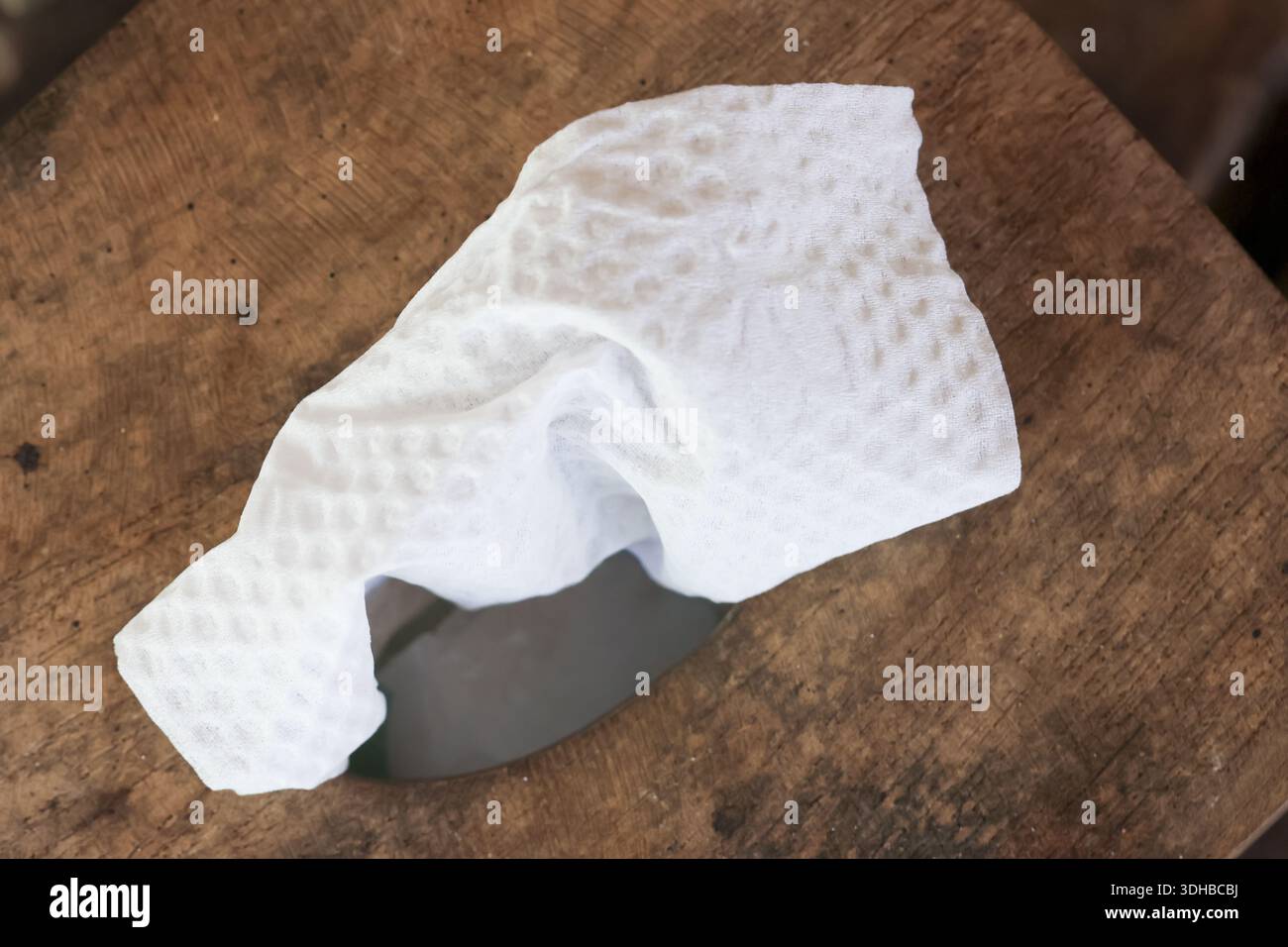 Crumpled white cleaning wipe with textured surface lying on dark weathered wooden table background showing contrast between clean hygiene supply and r Stock Photo