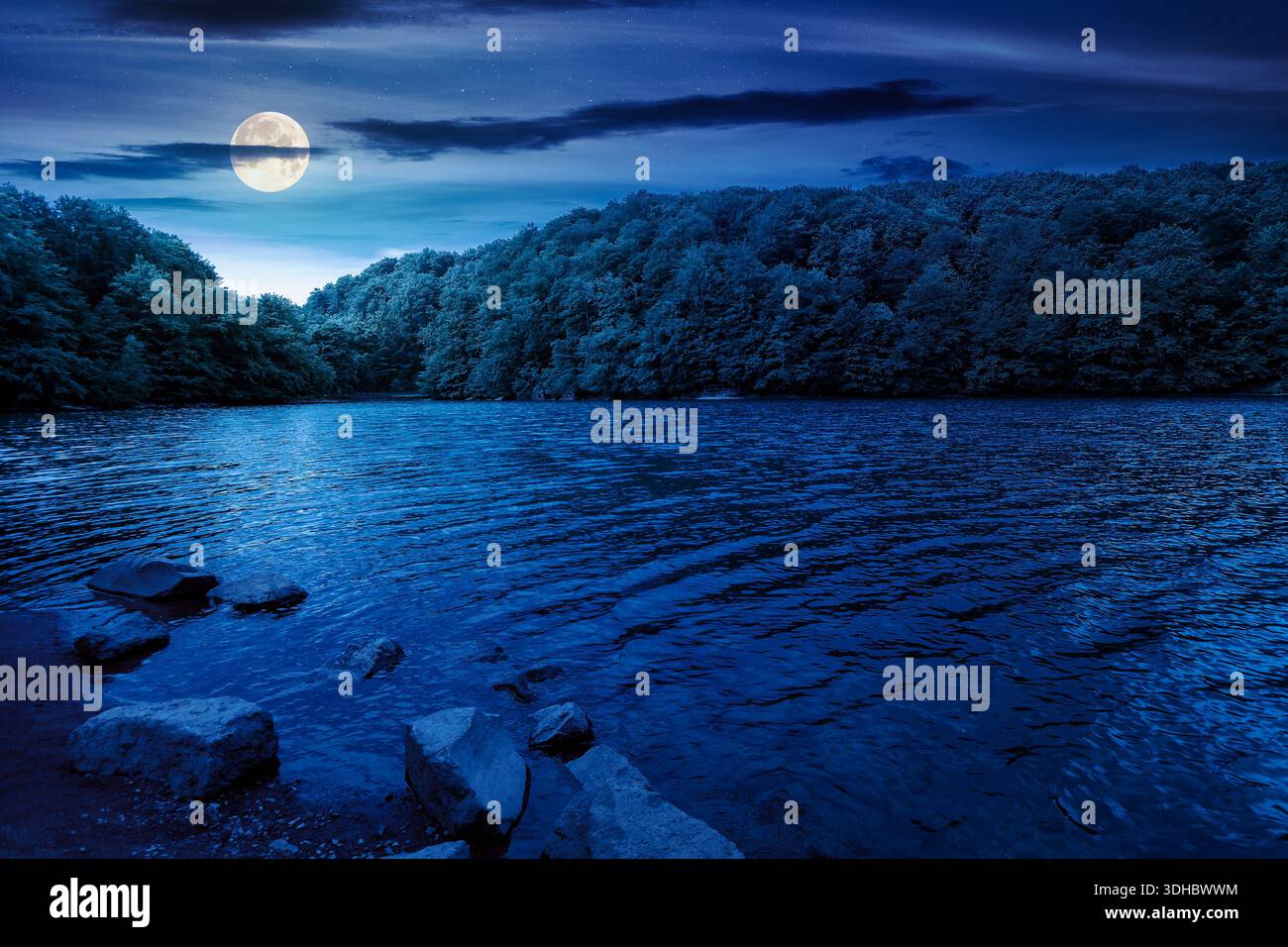 beautiful view of landscape with lake at night. body of water among beech forest in mountains in full moon light. summer weather with clouds on the sk Stock Photo