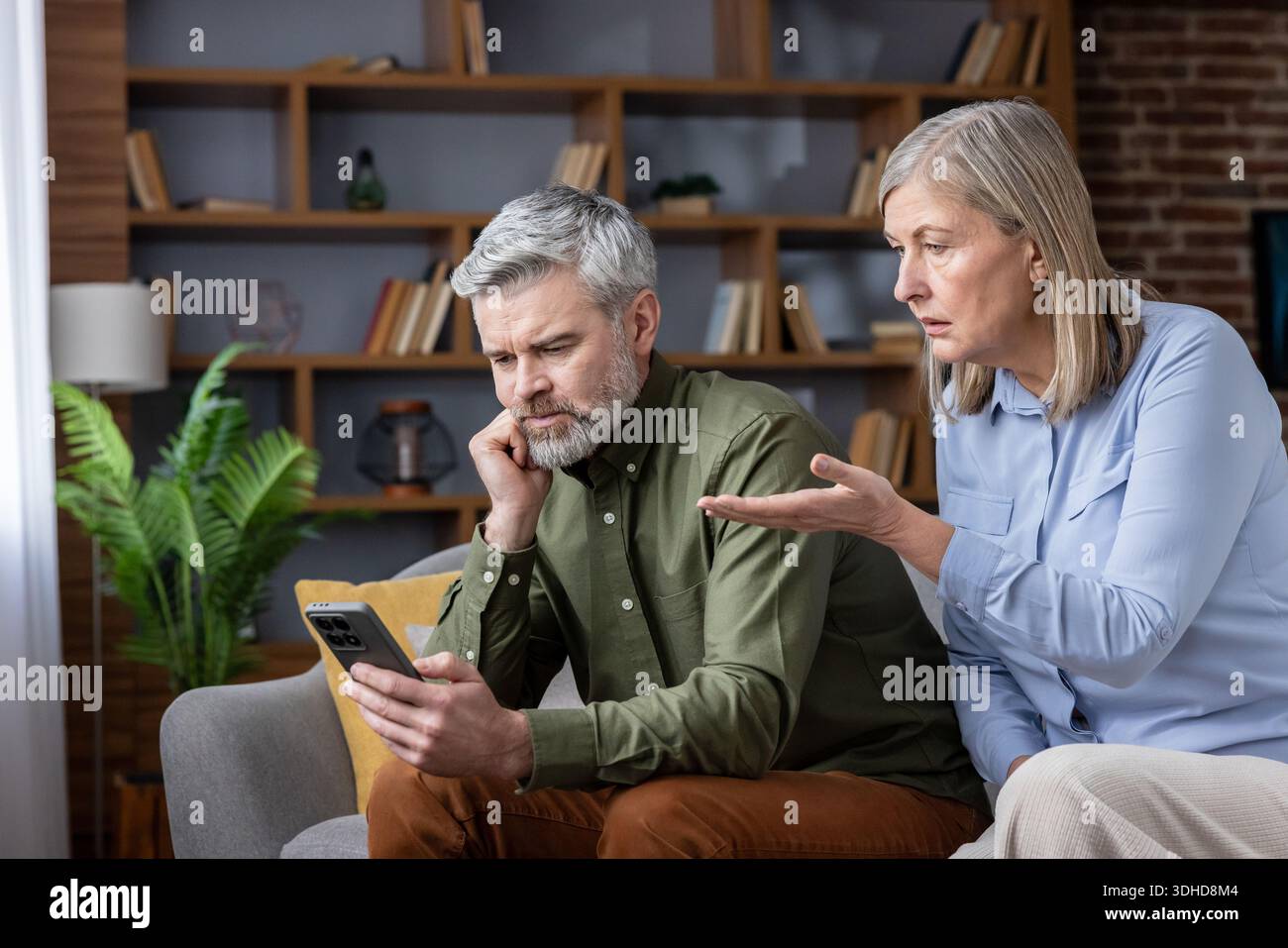 Mature couple having a disagreement while the man is distracted by his smartphone, highlighting issues of neglect and communication problems in their relationship at home Stock Photo