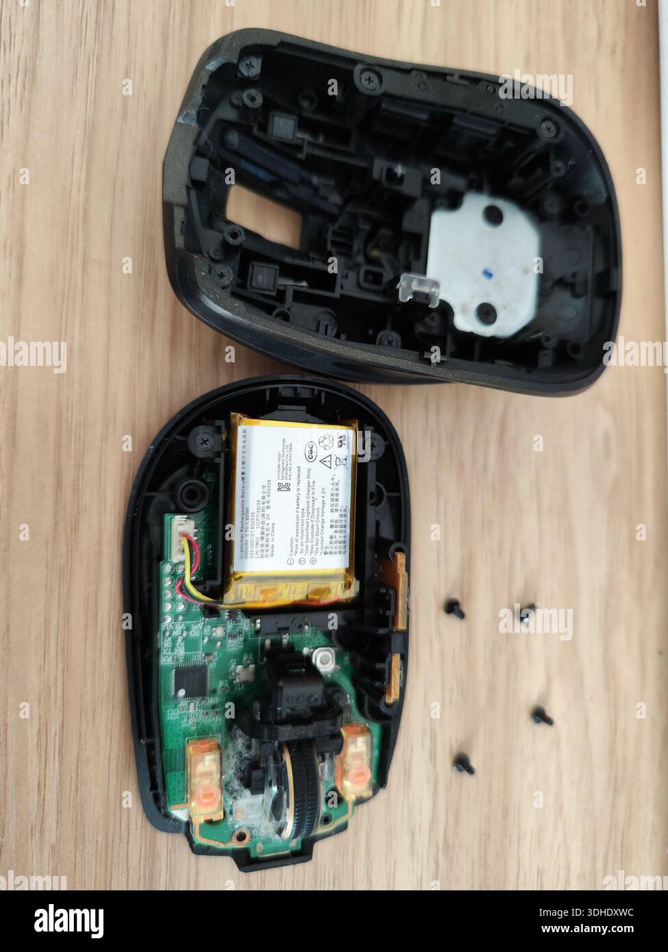 Disassembled computer mouse showing internal components and screws on wooden surface Stock Photo