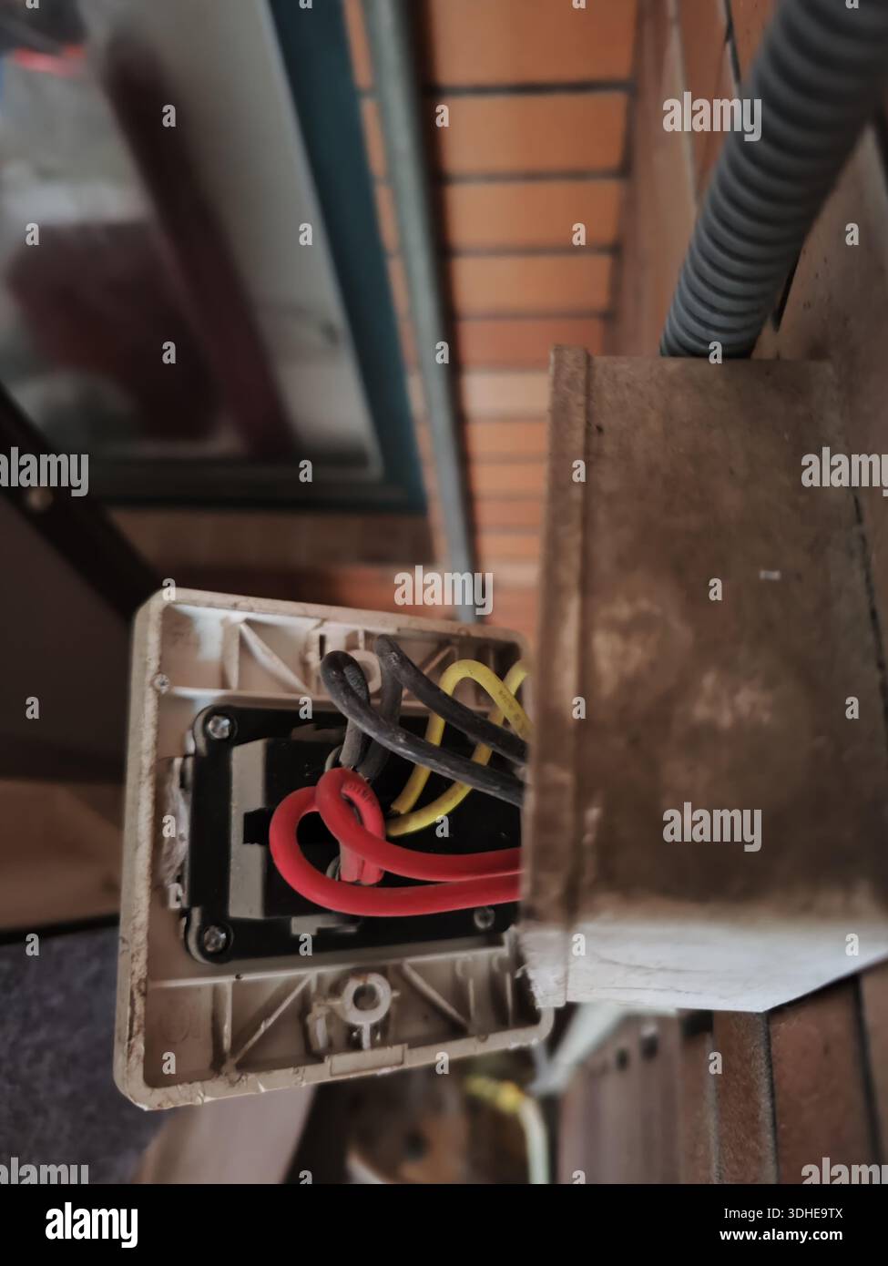 Open electrical junction box with wires exposed on a brick wall Stock Photo