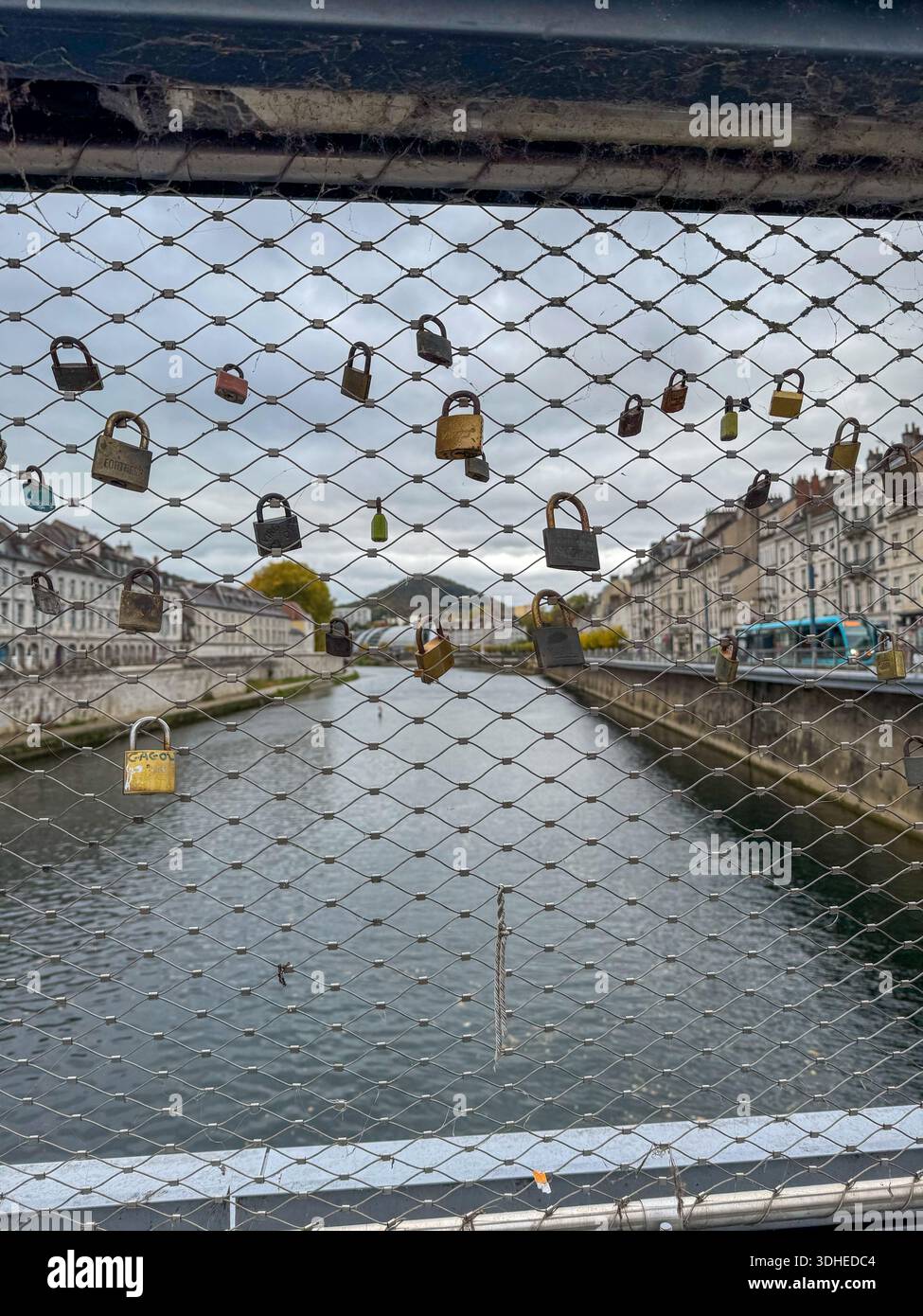 close up of love locks attached to the wire mesh of a pedestrian bridge in besançon, France. the doubs river, city buildings, blue tramway are visible - Smartphone Captured Stock Image