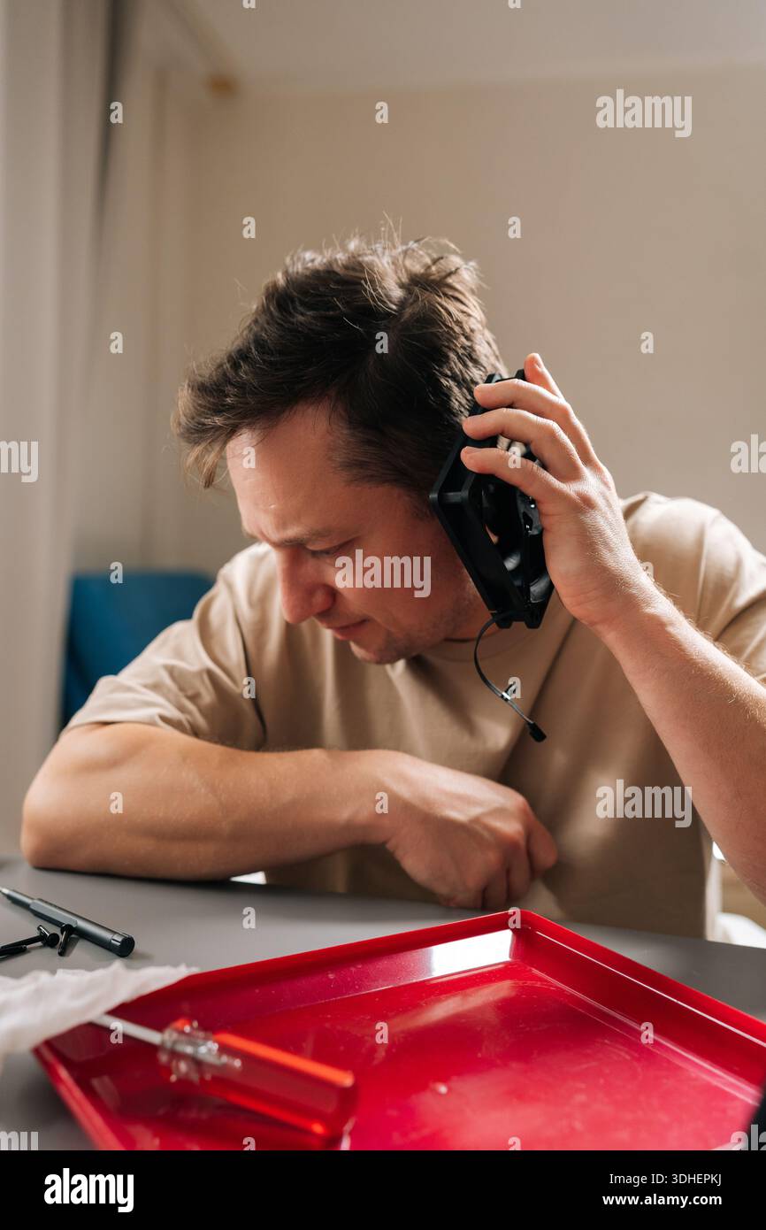 Man repairing computer cooling system, holding components, demonstrating expertise and focus fixing hardware issues at home office. Concept of Stock Photo