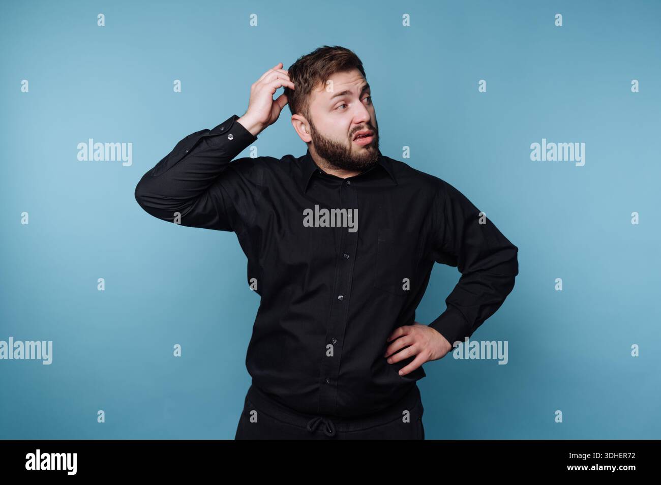 Man in black shirt scratching head with confused expression Stock Photo